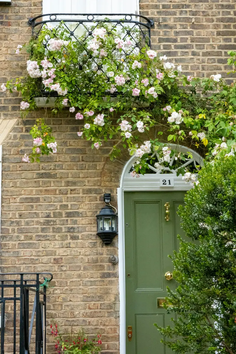 A green front door on a brick house with climbing roses